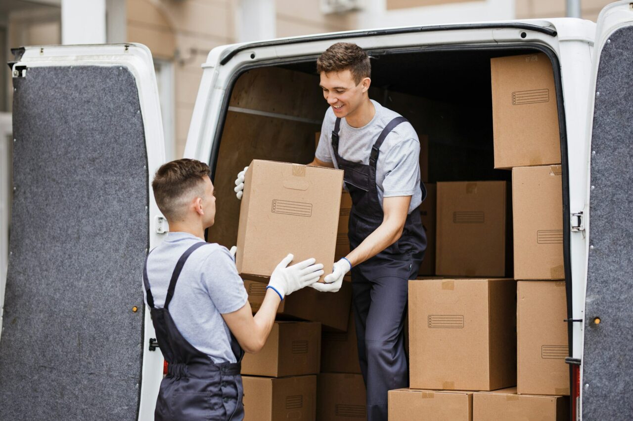 Two young handsome movers wearing uniforms are unloading the van full of boxes. House move, mover